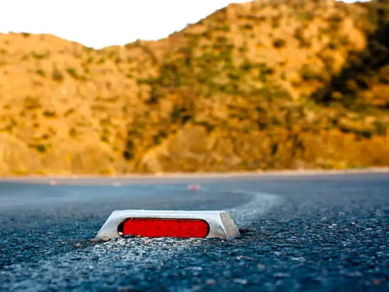Red reflective road marker embedded in asphalt highway curve for lane guidance and nighttime driving safety.