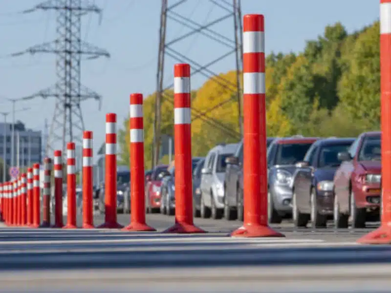 Orange traffic delineator posts used for lane separation and safety control on busy roadway with vehicles lined up.