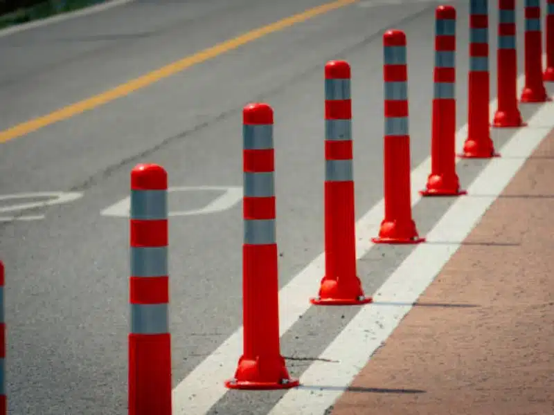 Orange traffic safety delineator posts with reflective bands providing lane separation and pedestrian safety on road.