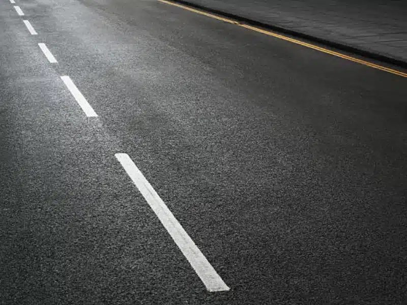 Smooth asphalt roadway with new white dashed lane markings and yellow curb line, highlighting professional pavement striping work