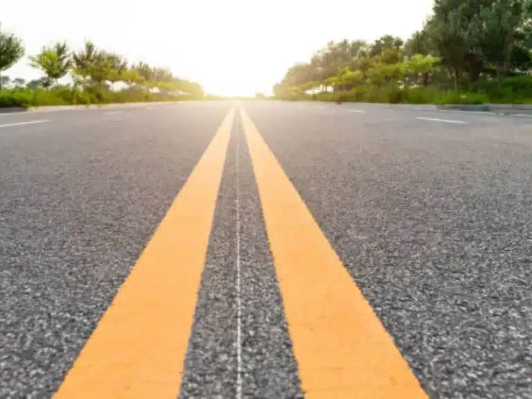 Low-angle view of asphalt road with bright yellow double center lines leading toward the horizon at sunrise.