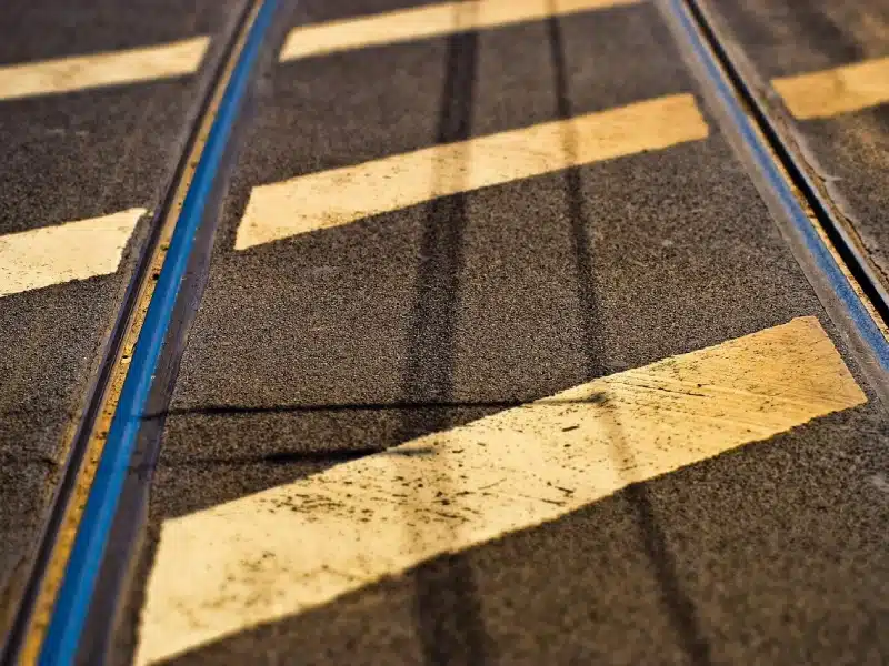 Pavement close-up showing yellow diagonal traffic markings on asphalt roadway with embedded rail tracks.